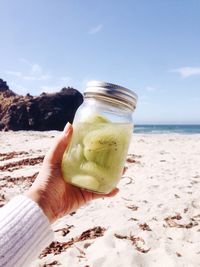 Cropped hand holding jar with kiwis at beach