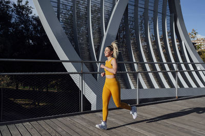 Smiling young athlete jogging on footbridge