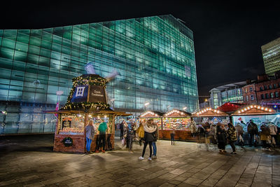 People at illuminated city against sky at night