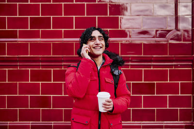 Portrait of smiling young woman standing against red wall