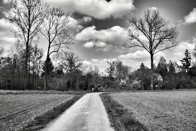Road passing through field against cloudy sky