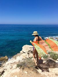 Rear view of woman holding sarong while standing on shore at beach