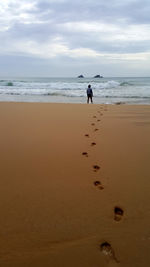 Footprints leading towards man standing on beach