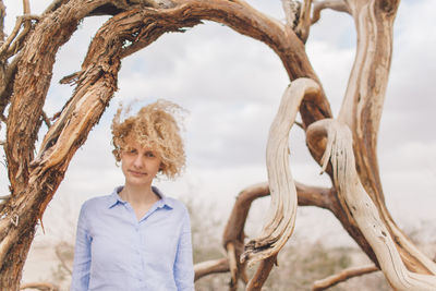 Young woman standing by tree trunk against sky