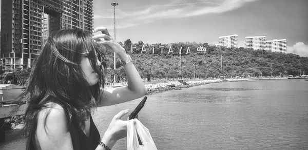 Woman photographing by modern buildings in city against sky