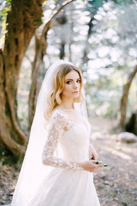 Portrait of young woman standing against trees