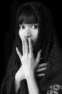 Portrait of shocked young woman covering mouth against black background