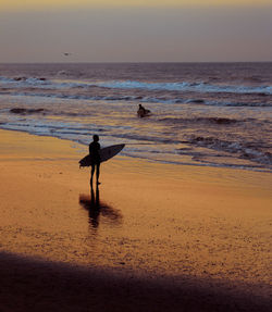 Silhouette men on beach against sky during sunset