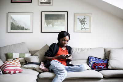 Mid adult woman using smart phone on sofa at home