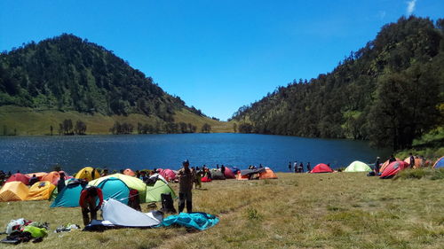 Group of people on shore by lake against blue sky