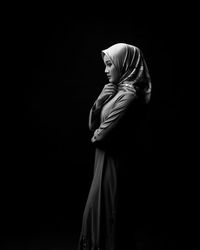 Side view of woman standing against black background