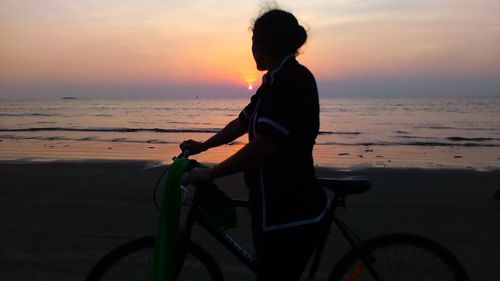 Woman on bicycle at beach during sunset