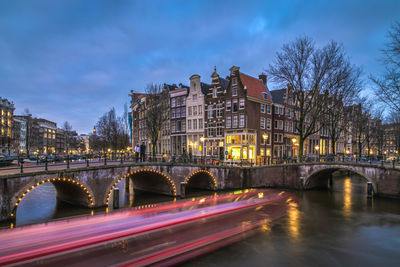 Illuminated bridge over river in city against sky at dusk