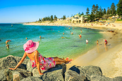 Rear view of woman sitting on rocks by beach