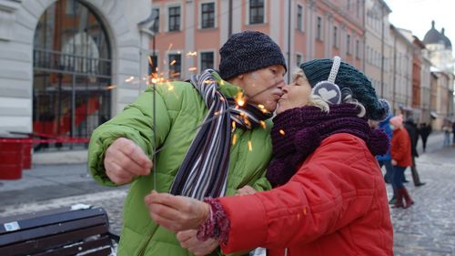 Senior couple holding sparkler while kissing outdoors