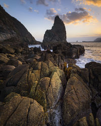 Rocks on shore against sky during sunset