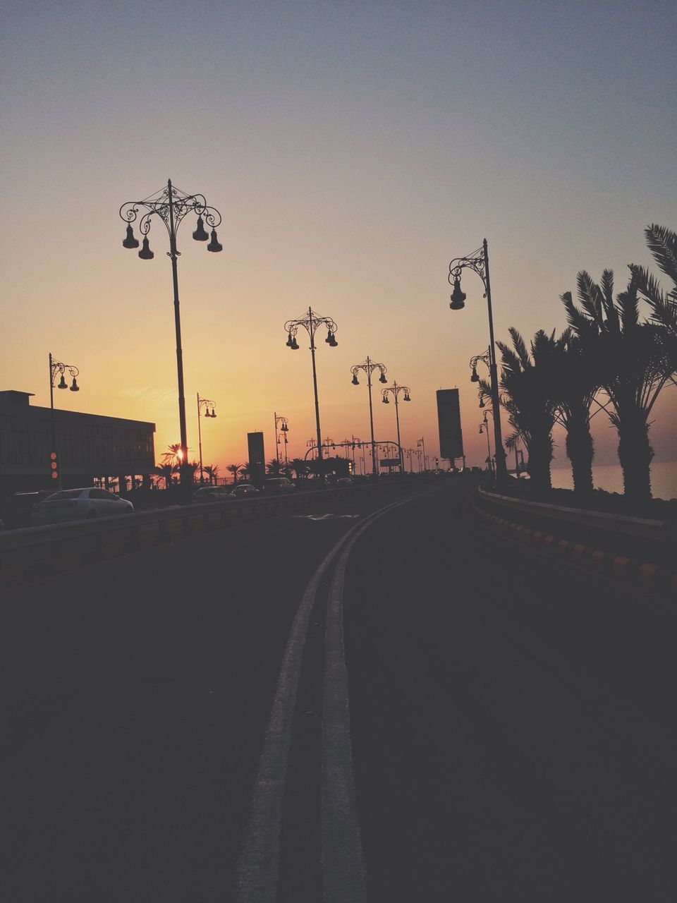 sunset, transportation, the way forward, road, silhouette, street light, tree, car, street, clear sky, sky, diminishing perspective, road marking, vanishing point, mode of transport, land vehicle, dusk, palm tree, outdoors, empty