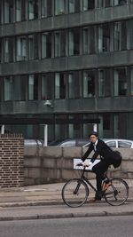Full length of man riding bicycle against building in city