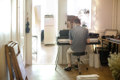 Rear view of man playing piano at home