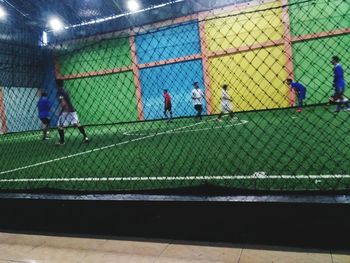 People playing soccer on field seen through chainlink fence