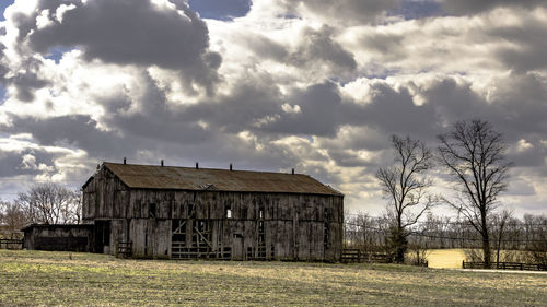Abandoned barn on field against cloudy sky