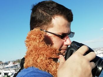 Close-up portrait of man holding camera against sky