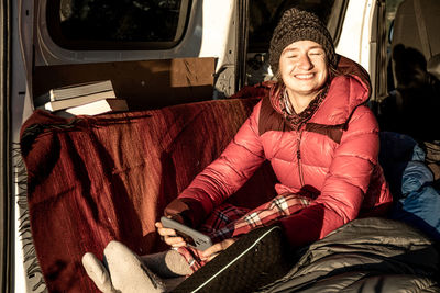 Girl wrapped up in pink feathers smiling at sunrise in her campervan