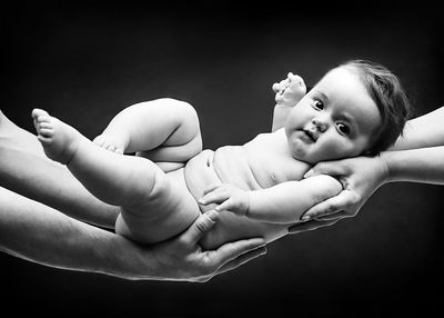 Portrait of cute shirtless toddler held by cropped hands