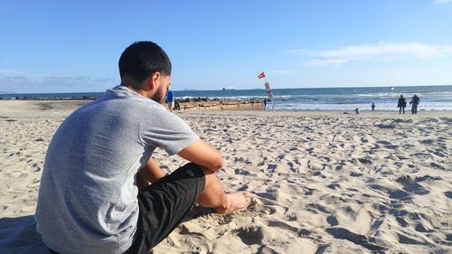 Full length of man sitting at beach against sky