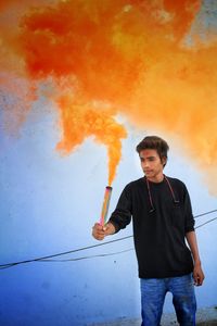 Man holding distress flare while standing against wall