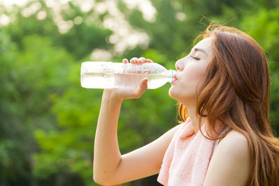 Woman drinking water from bottle against trees