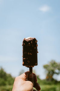 Hand holding ice cream cone against sky