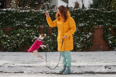 Full length of woman with dog on snow covered road