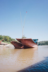 Abandoned boat moored in lake against clear blue sky
