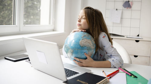 Girl looking away while sitting on table at home