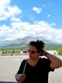 Portrait of young woman wearing sunglasses standing on mountain against sky