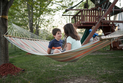 Happy siblings talking while relaxing on hammock at yard