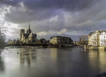 Notre dame cathedral by seine river against cloudy sky