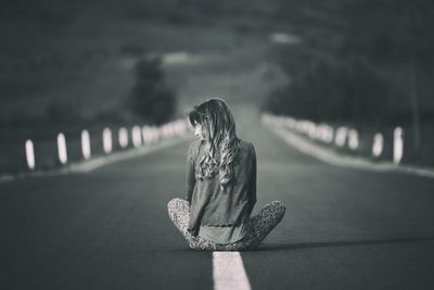 Rear view of woman sitting on empty country road