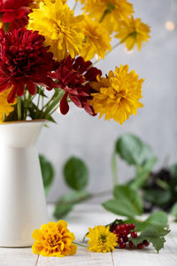 Bouquet of red and yellow flowers in jug on white table. autumn holiday concept.