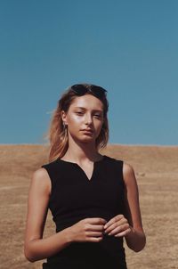 Beautiful young woman standing in desert against clear blue sky