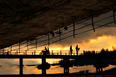 Silhouette people by railing against sky during sunset