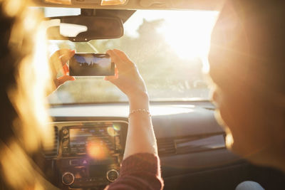 Man looking at woman photographing from mobile phone through car windshield