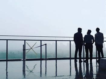 Rear view of silhouette friends standing in wet balcony during rainy season