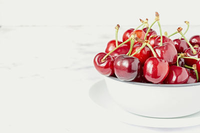 Fresh ripe red cherry with stalks in white ceramic pot placed on marble table against white wall