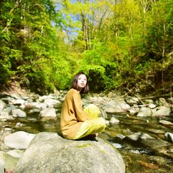 Woman sitting on rock against trees in forest