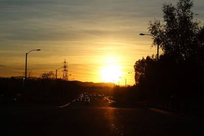 Road by silhouette trees against sky during sunset