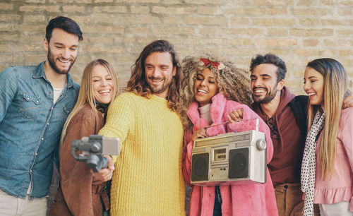 Friends taking selfie while standing against brick wall