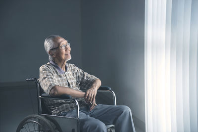 Senior man looking away while sitting on wheelchair at home