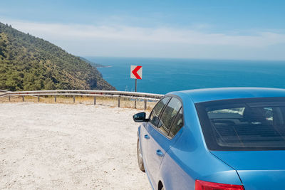 Blue car parked on the side of the road with a view to the calm mediterranean sea